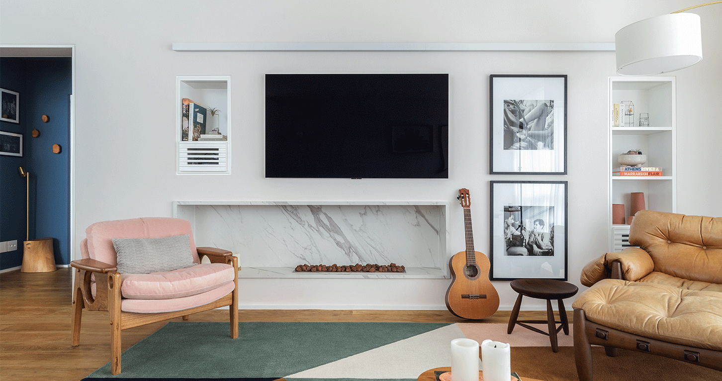Apartamento da Flavia, sala de estar e tv com lareira, poltronas, quadros, mesa lateral, tapete e piso de madeira