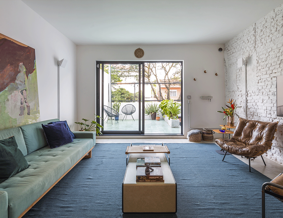Casa do Marcos e da Júlia, sala de estar, poltronas, sofá, tapete azul, parede tijolinho branca, terraço com plantas