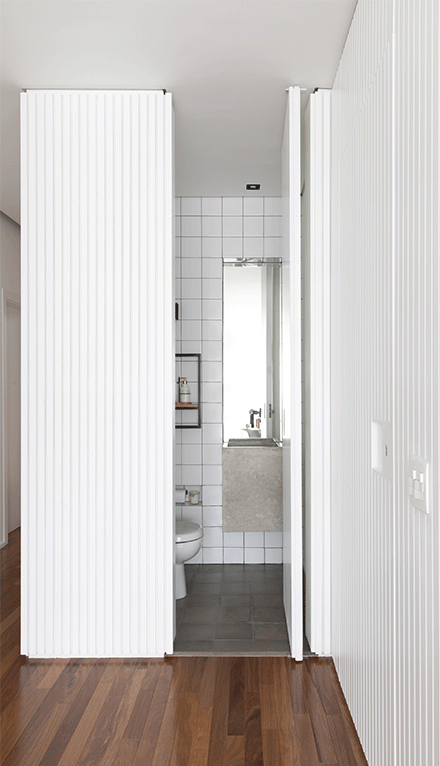 Apartamento Edu e Clarissa painel ripado branco, porta mimetizada, lavabo, piso de madeira