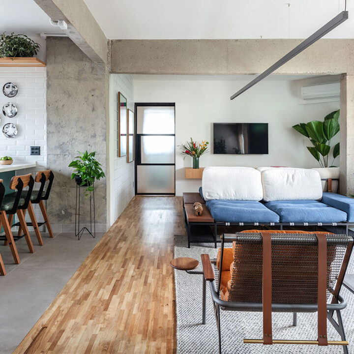 Sala integrada do Apartamento Gomes de Carvalho, com piso de madeira, sofá azul e pilares de concreto aparente, na Vila Olímpia