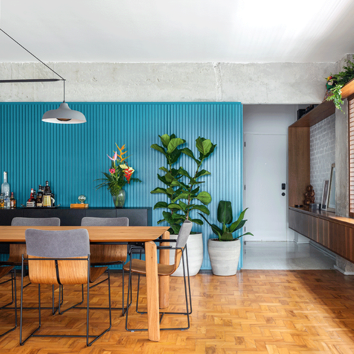 Sala de jantar do Apartamento Jardins, com parede ripada azul, mesa de madeira e piso de taco, nos Jardins