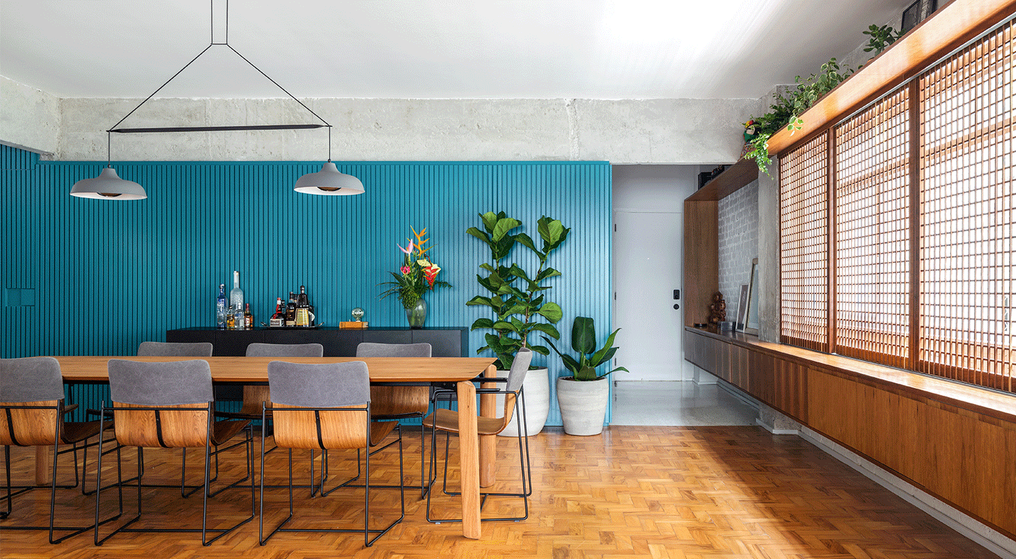 Sala de jantar do Apartamento Jardins, com parede ripada azul, mesa de madeira e piso de taco, nos Jardins