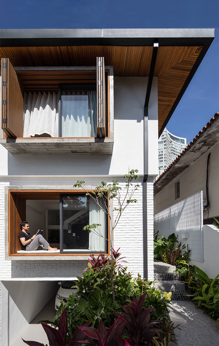 Fachada da Casa Akama com janelas de madeira, tijolo branco e jardim tropical, em Pinheiros