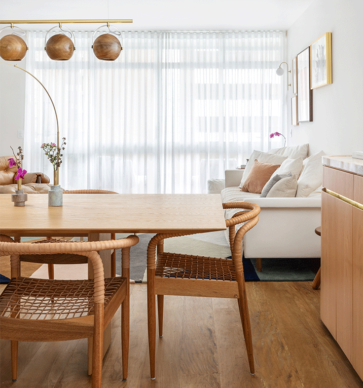 Mesa de jantar de madeira com cadeiras de palha no Apartamento Galeria, com sala ao fundo
