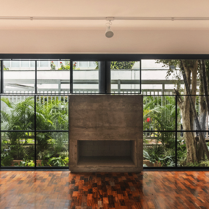 Sala da Casa Lareira com lareira de concreto, piso de taco e grandes caixilhos voltados para o jardim, na Vila Beatriz